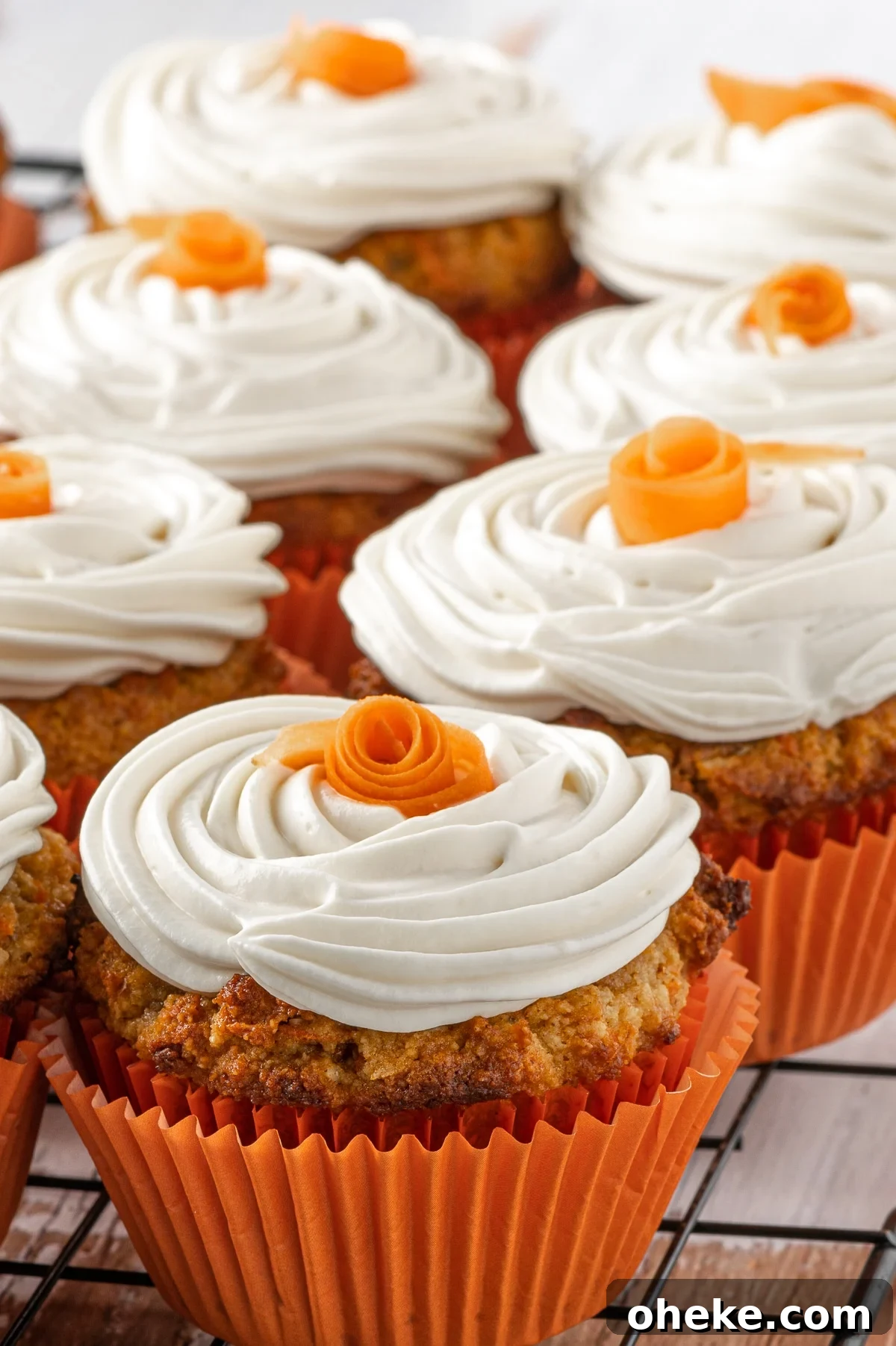 Close up of a batch of low carb carrot cake muffins with swirls of cream cheese frosting and small orange roses on the top. 