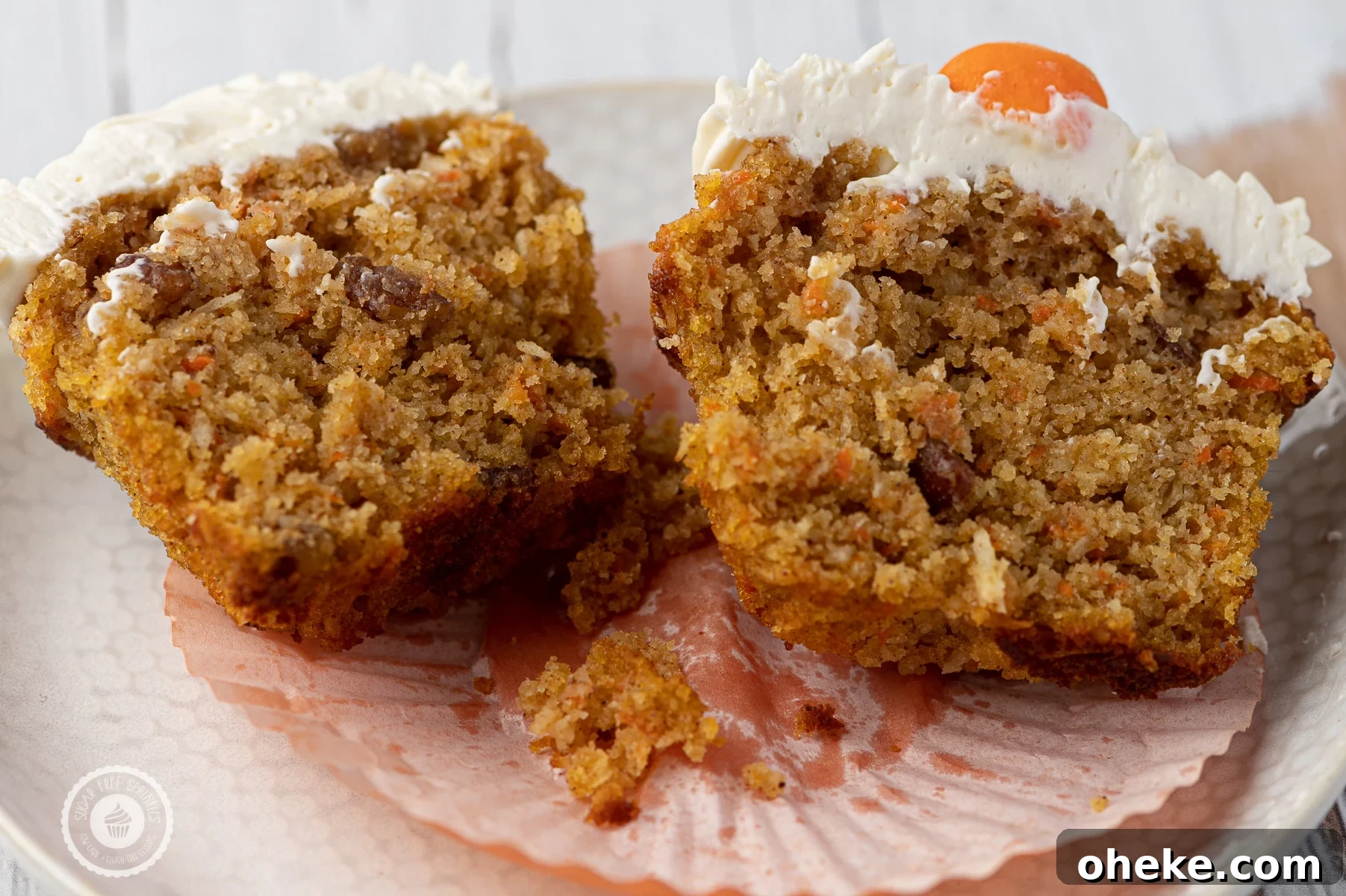 A carrot cake muffin with cream cheese frosting cut down the center and place on a white textured plate. 