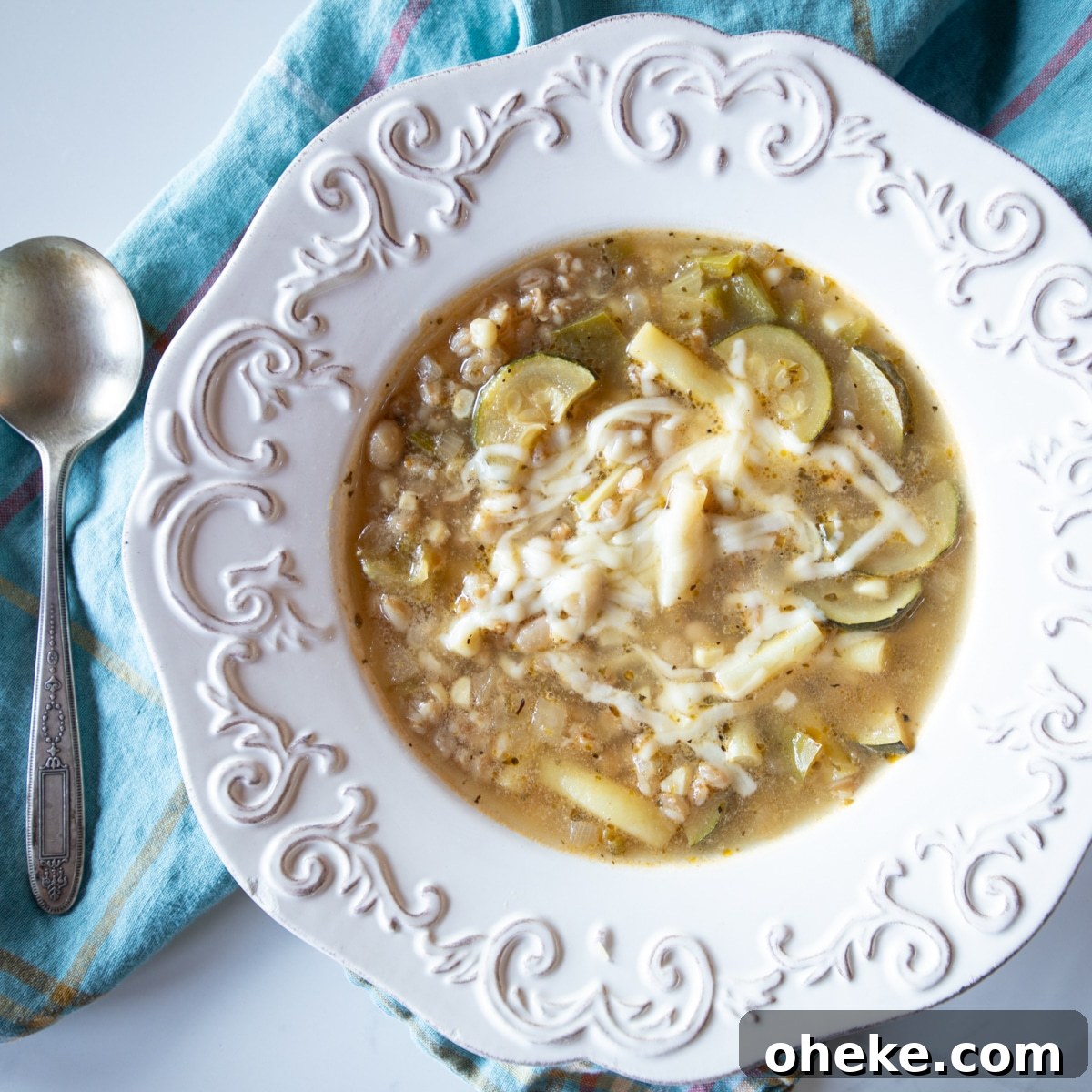 September Week 2 Vegetarian Meal Plan: Fresh Recipes & Grocery List 5 A bowl of summer vegetable soup topped with grated Swiss cheese on a tea towel with a spoon.
