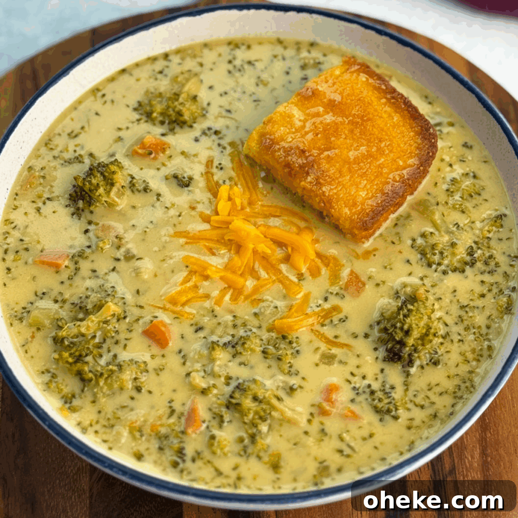 Slow Cooker Broccoli Cheddar Soup (Crockpot Recipe) 2 Overhead view of a bowl filled with creamy broccoli cheddar soup, chunks of broccoli and carrots, a sprinkle of shredded cheddar, and a piece of cornbread resting in the soup.