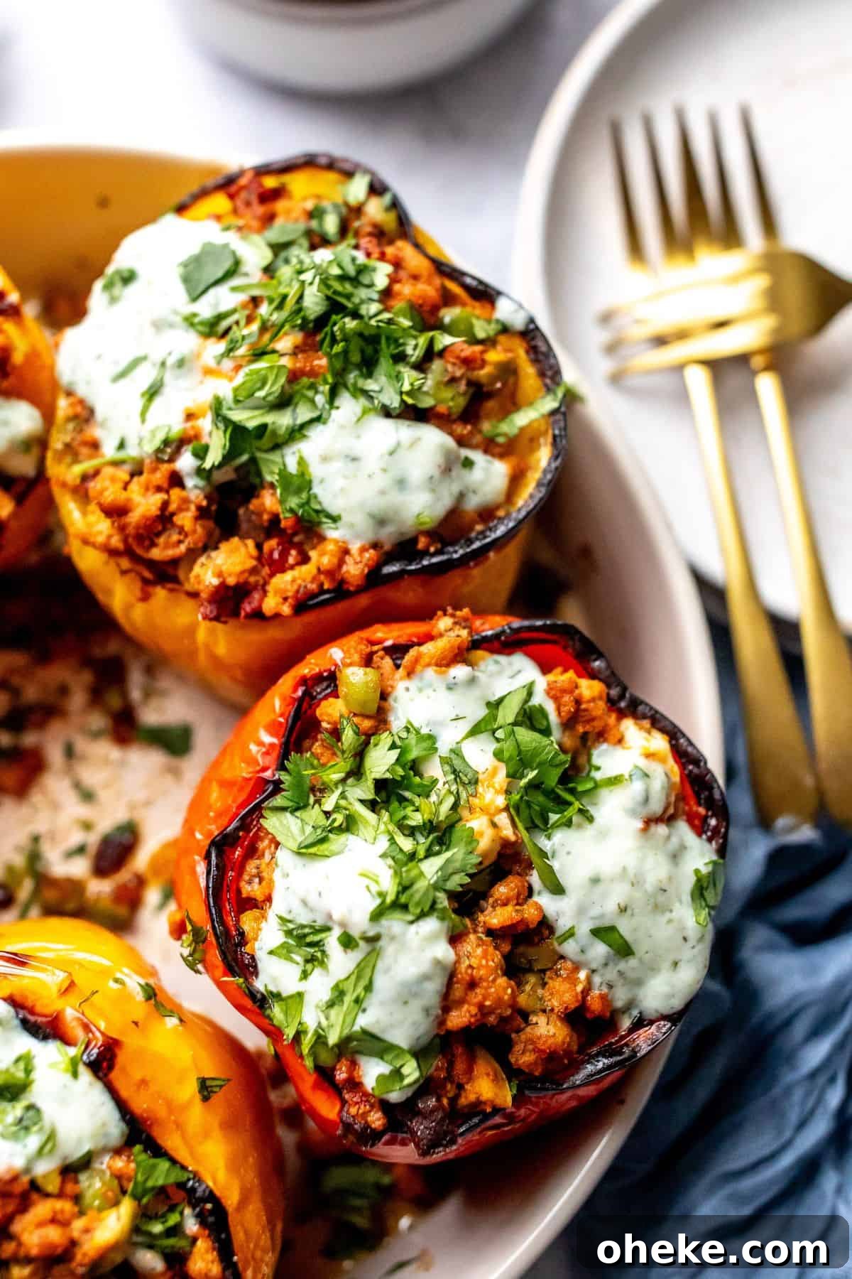 Mediterranean Stuffed Peppers with Ground Turkey and Feta 5 Ground turkey stuffed Peppers in a grey bowl with gold forks and plates on the side. Up close photo.