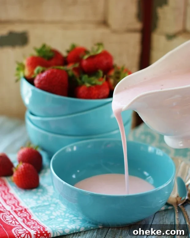 Completed strawberry bisque being poured into turquoise bowls with strawberries in the background.