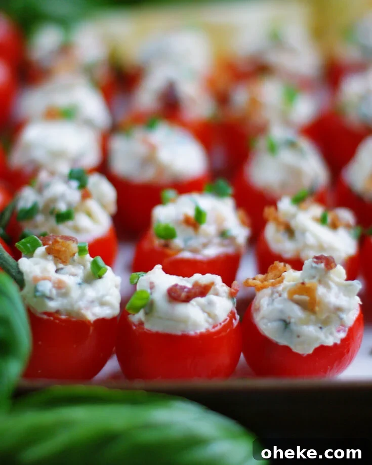 A party platter filled with cored cherry tomatoes stuffed with cream cheese, fresh herbs and bacon.
