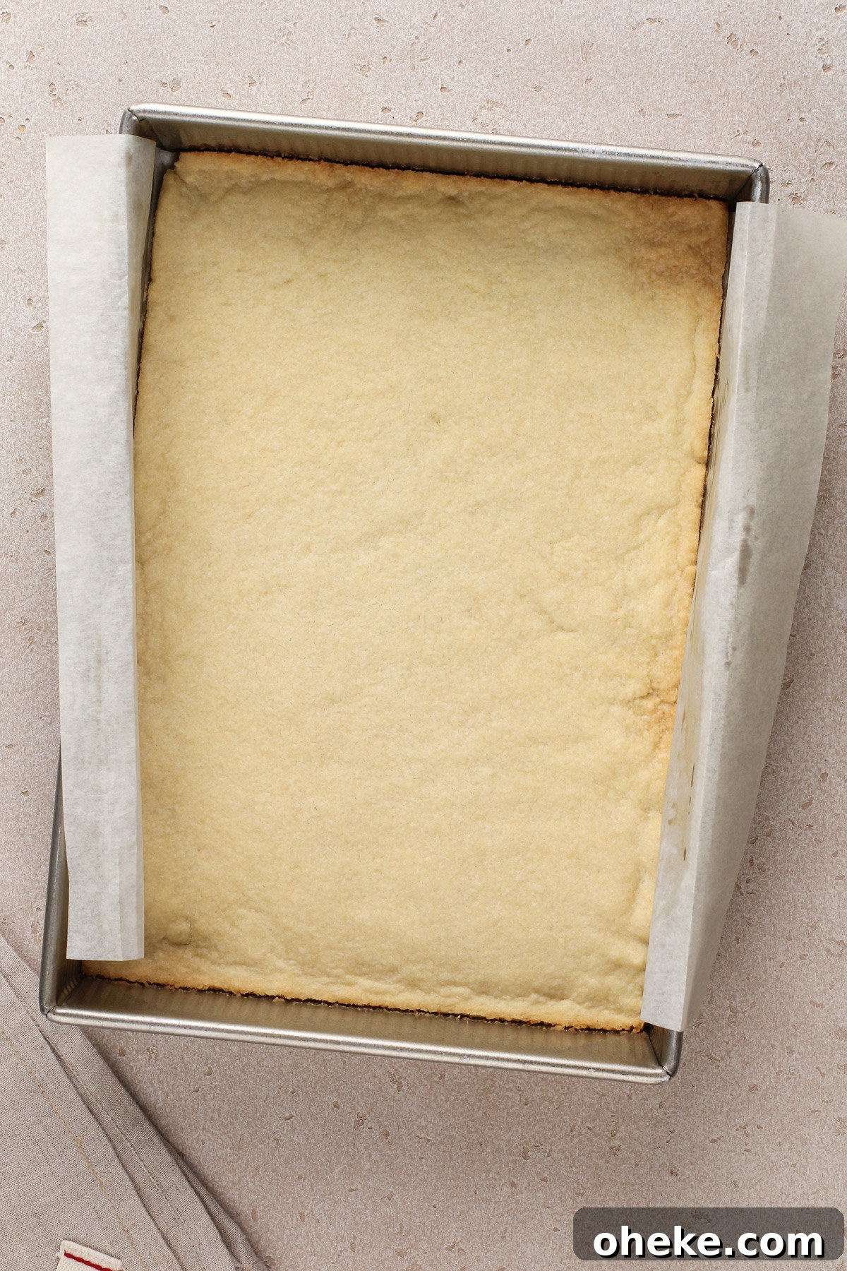 Baked crust for layered cherry cheesecake dessert in the bottom of a parchment-lined baking pan.