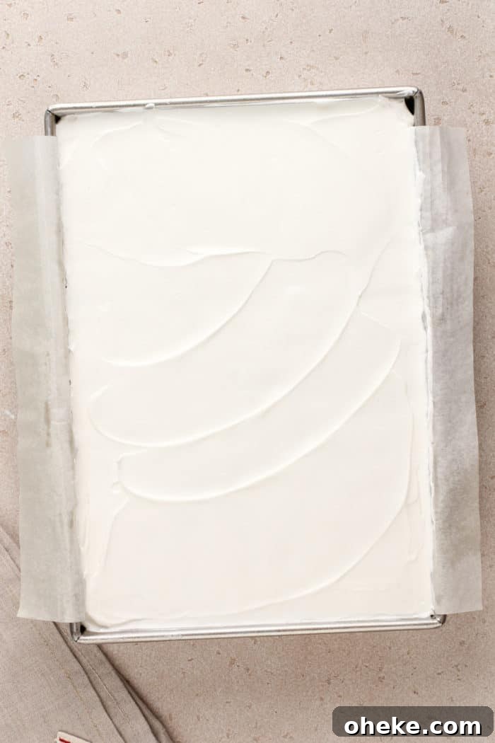 Assembled layered cherry cheesecake dessert in a parchment-lined baking pan, ready to be chilled.