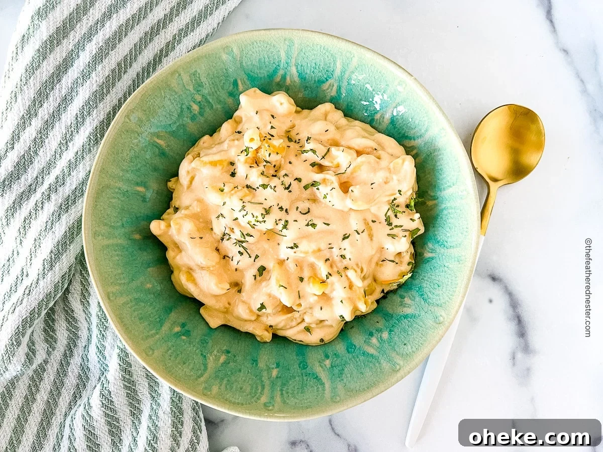 Creamy Slow Cooker Macaroni and Cheese Recipe 8 horizontal photo of slow cooker mac and cheese with cream cheese in a green bowl with a spoon at the side.