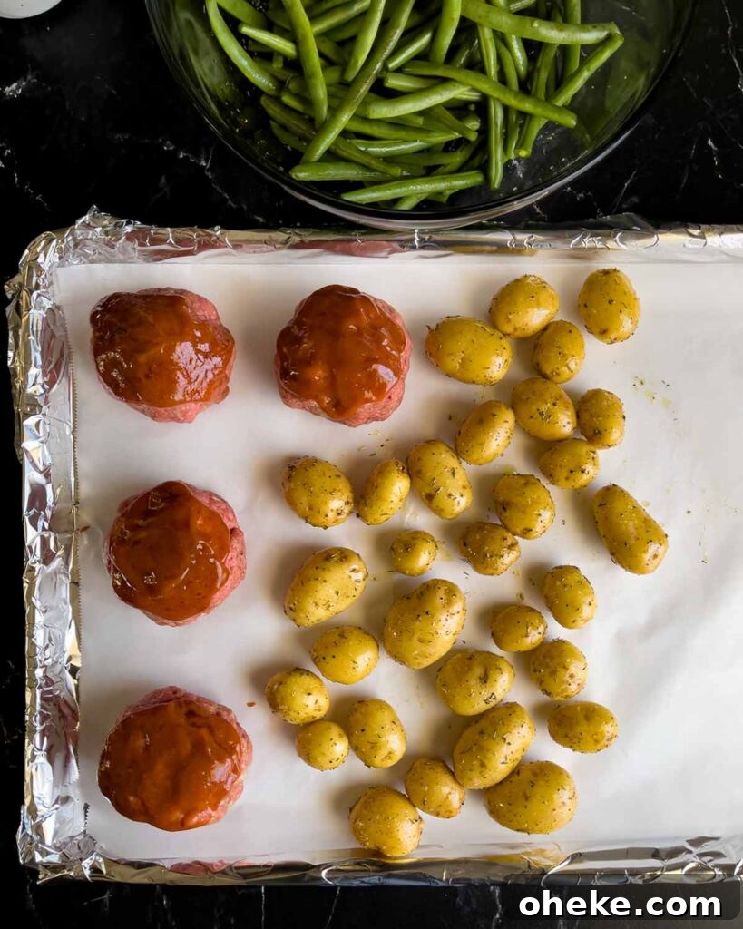 Potatoes added to the sheet pan with the mini meatloaves with the green beans in the background.