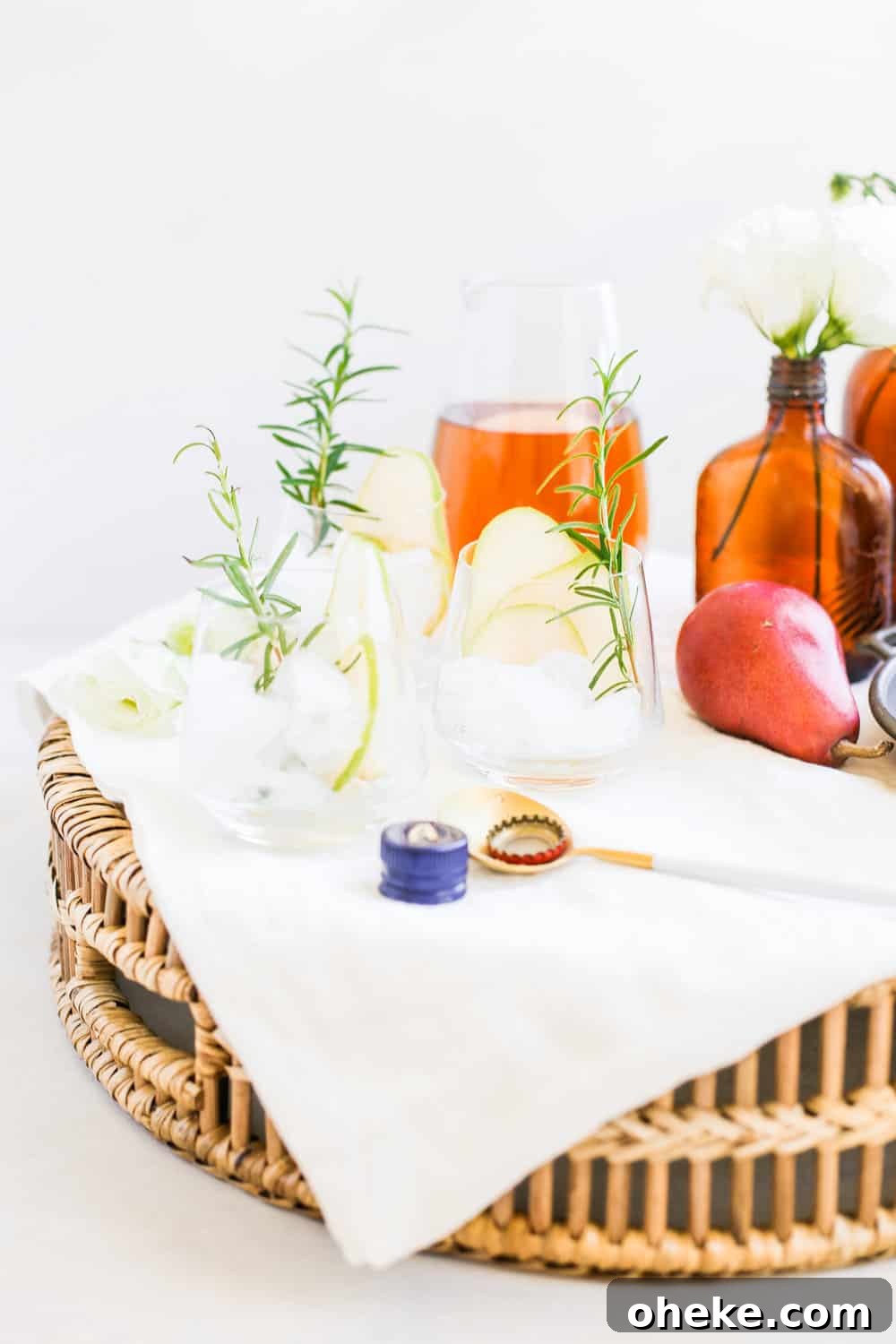 Low clear glasses garnished with a sliced pear, a sprig of rosemary, and ice on a serving tray.