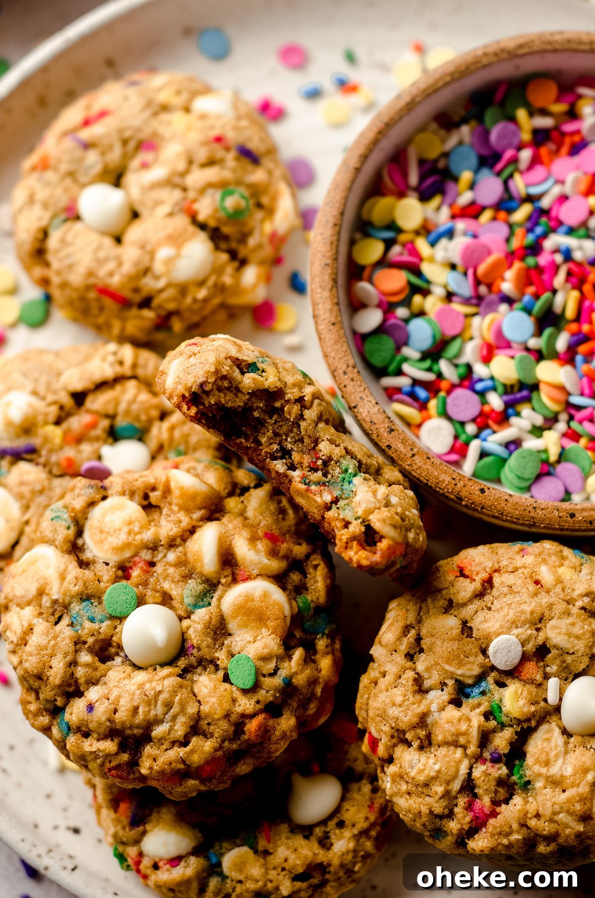 Funfetti White Chocolate Oatmeal Cookies Recipe 10 funfetti oatmeal cookies on a plate with a bowl of sprinkles and one cookie has a bite taken out of it
