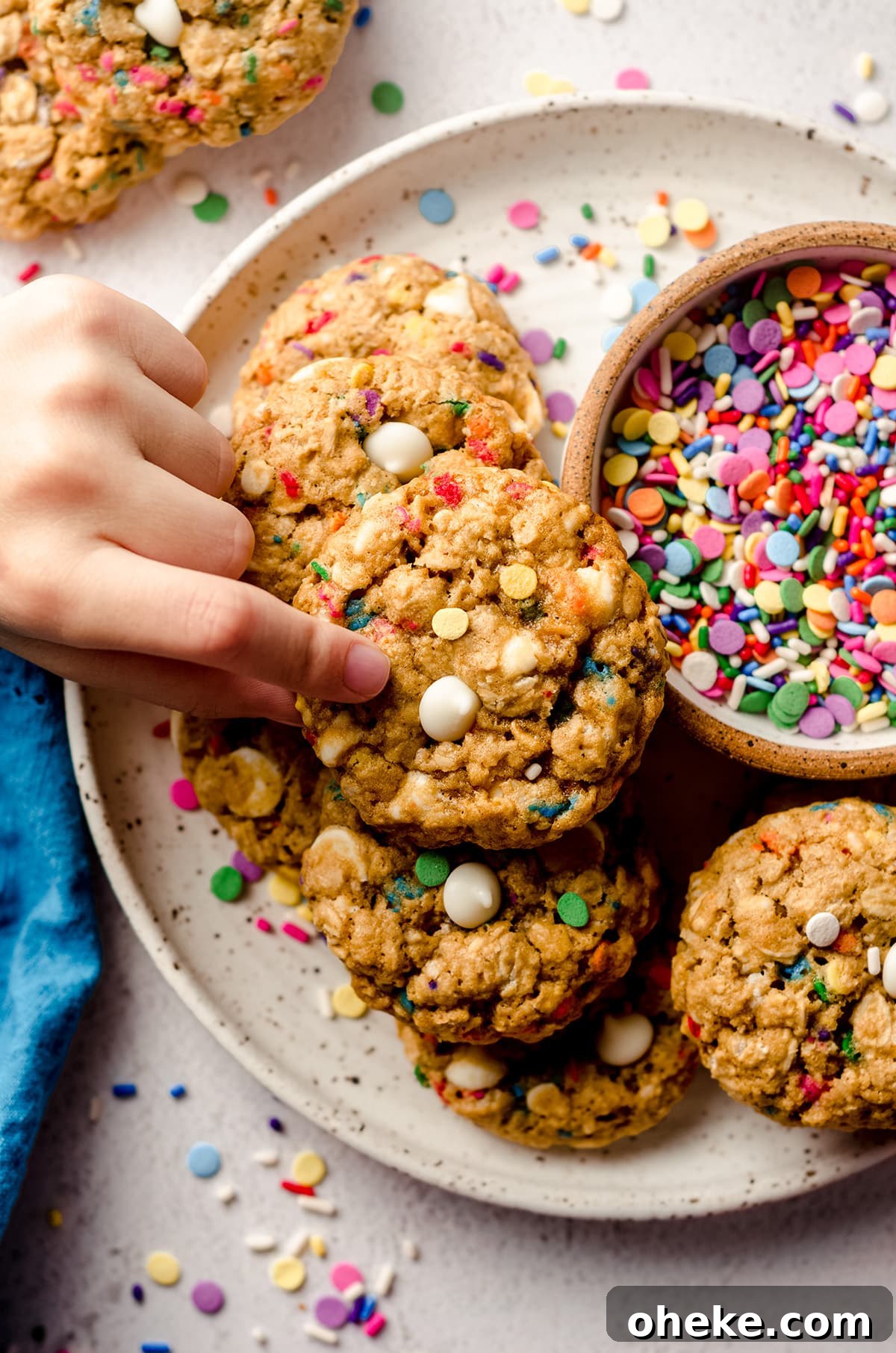 Funfetti White Chocolate Oatmeal Cookies Recipe 3 aerial photo of a child's fingers picking up a funfetti oatmeal cookie up from a plate of cookies