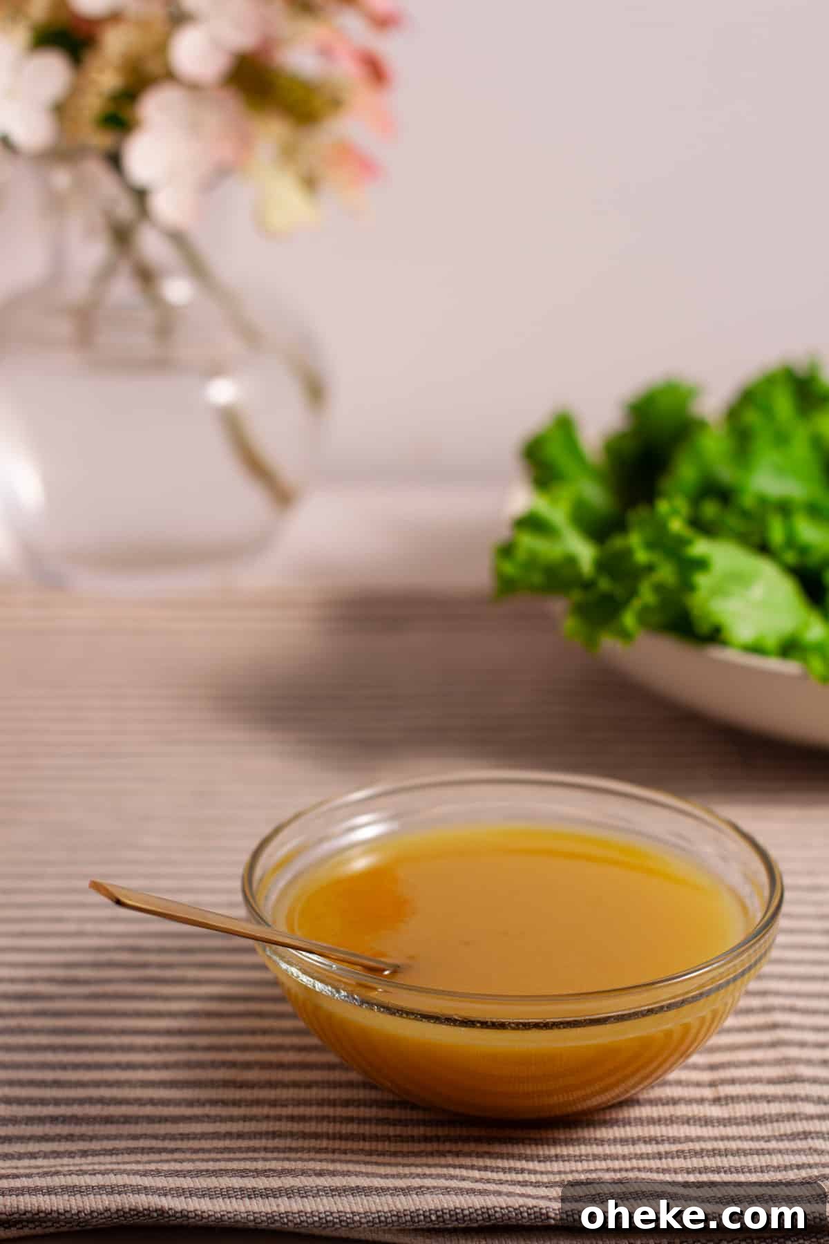 Maple Dijon Dressing in a small bowl on a table with a salad and flowers in the background.