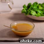 Maple Dijon Dressing in a small bowl on a table with a salad and flowers in the background.