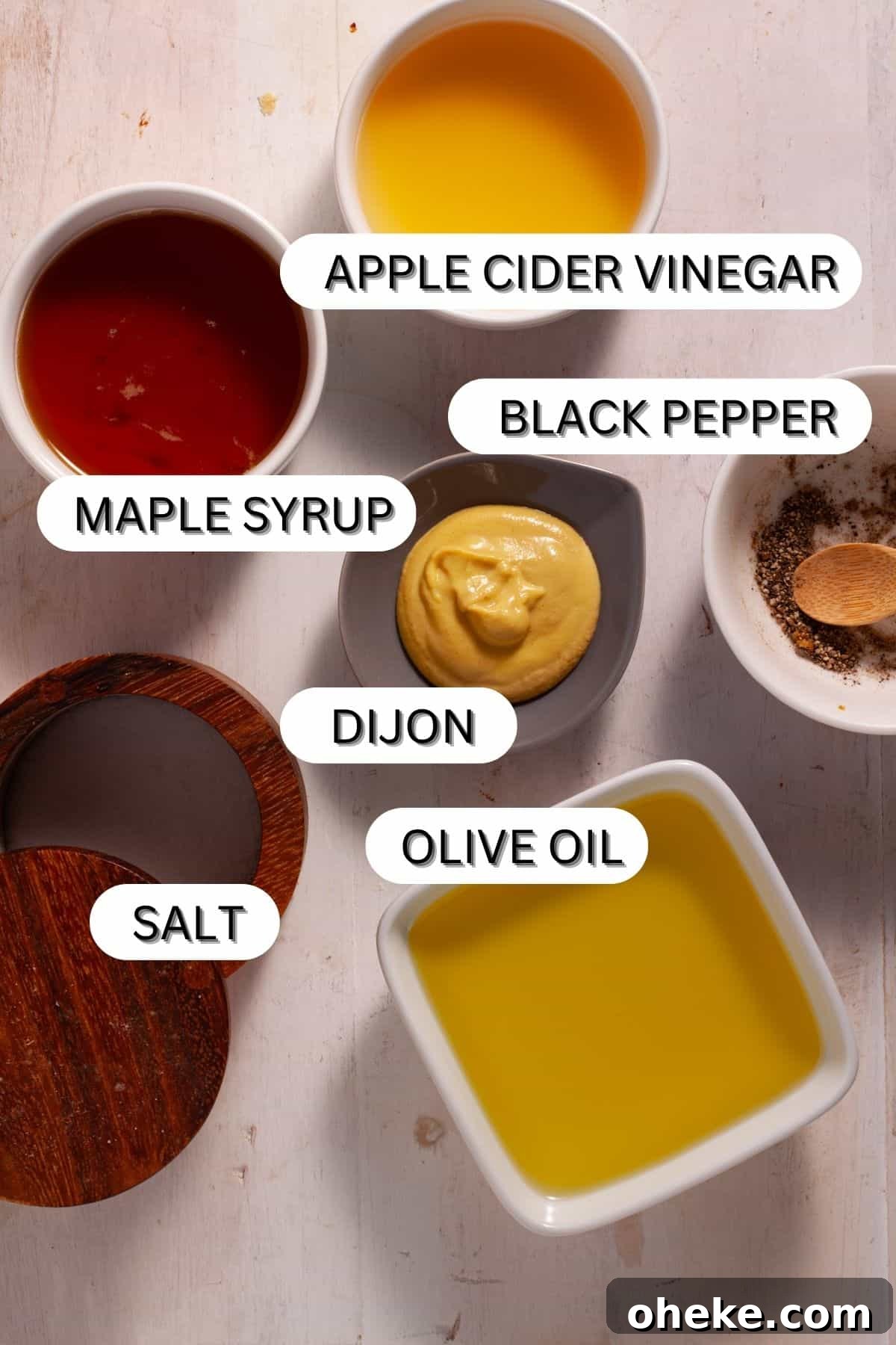Ingredients for maple dijon dressing in small bowls on white table.