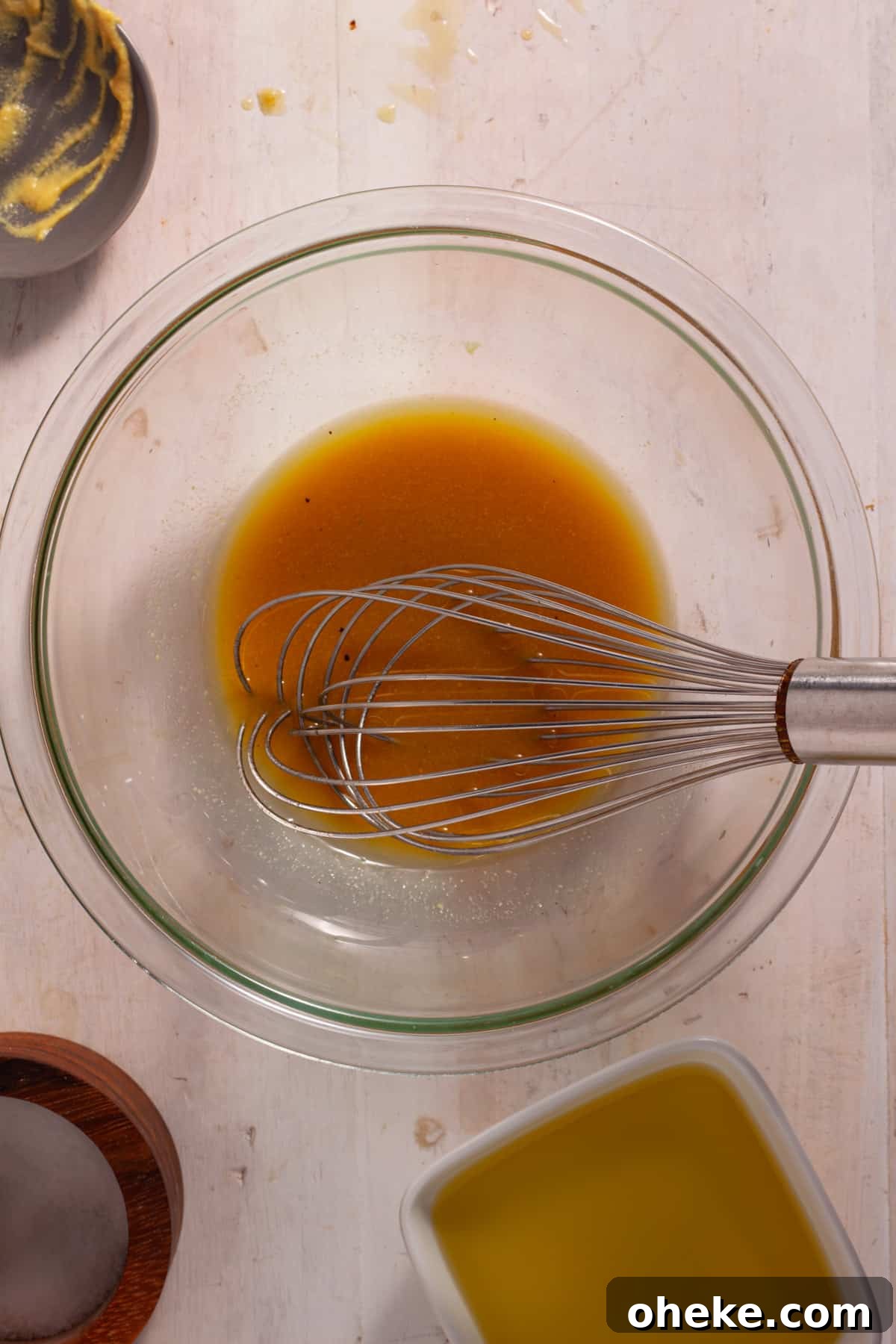 Maple Dijon Dressing getting whisked together in a medium bowl on a white table.