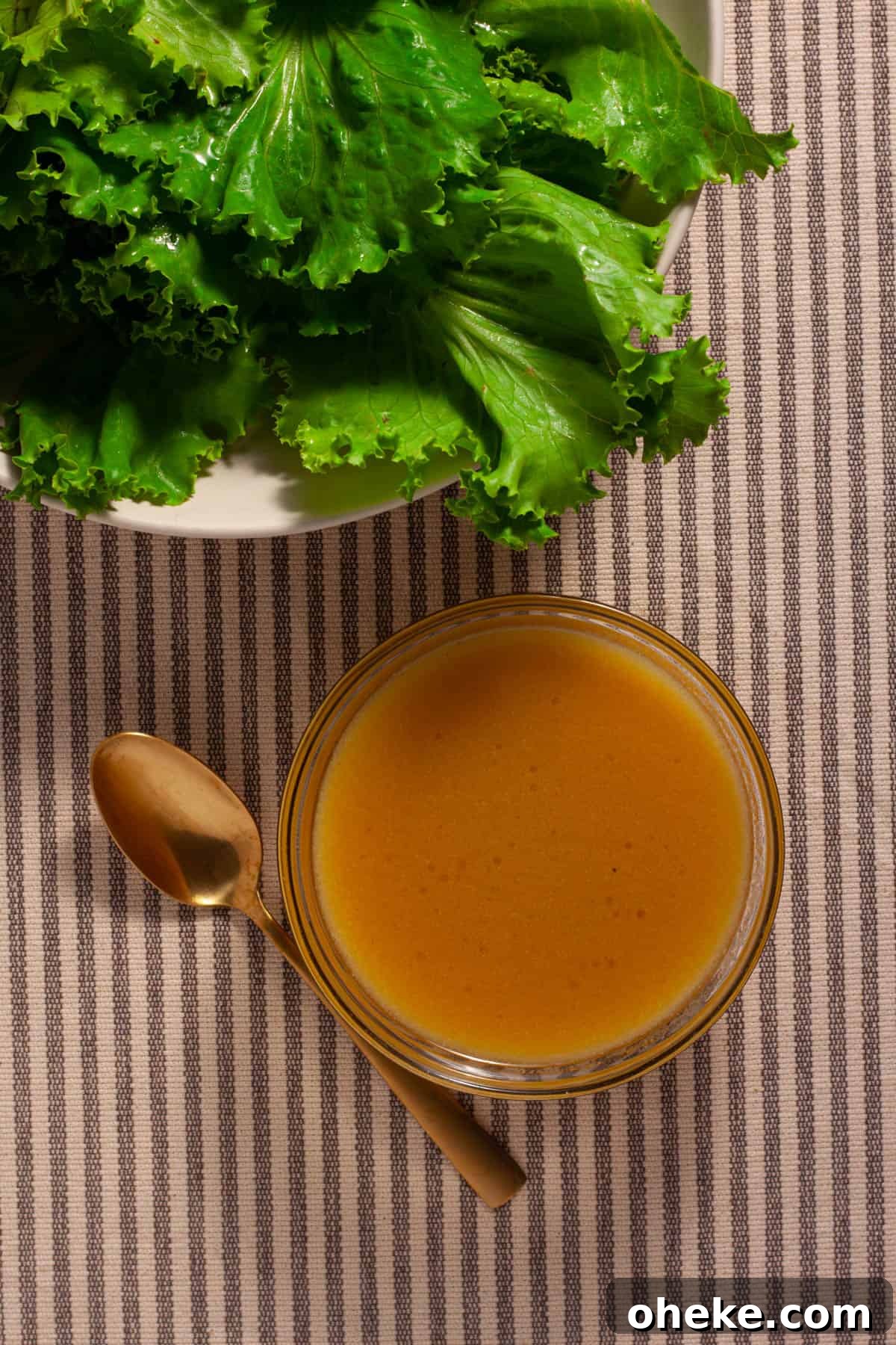 Maple Dijon Dressing in a small bowl on the side of a bowl of greens.