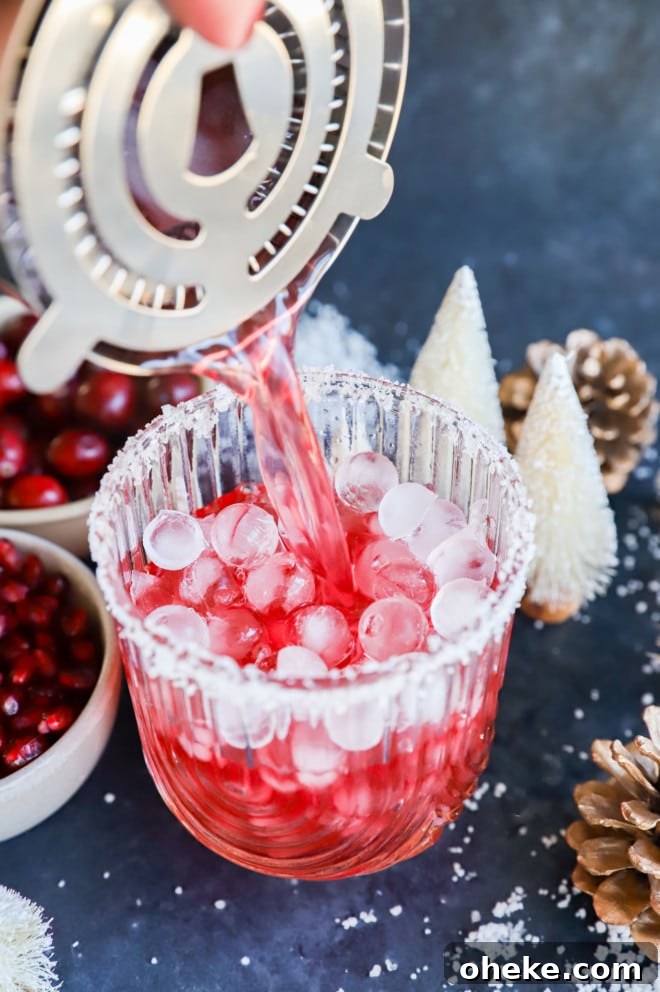 Pouring a cranberry pomegranate cocktail into a glass with ice