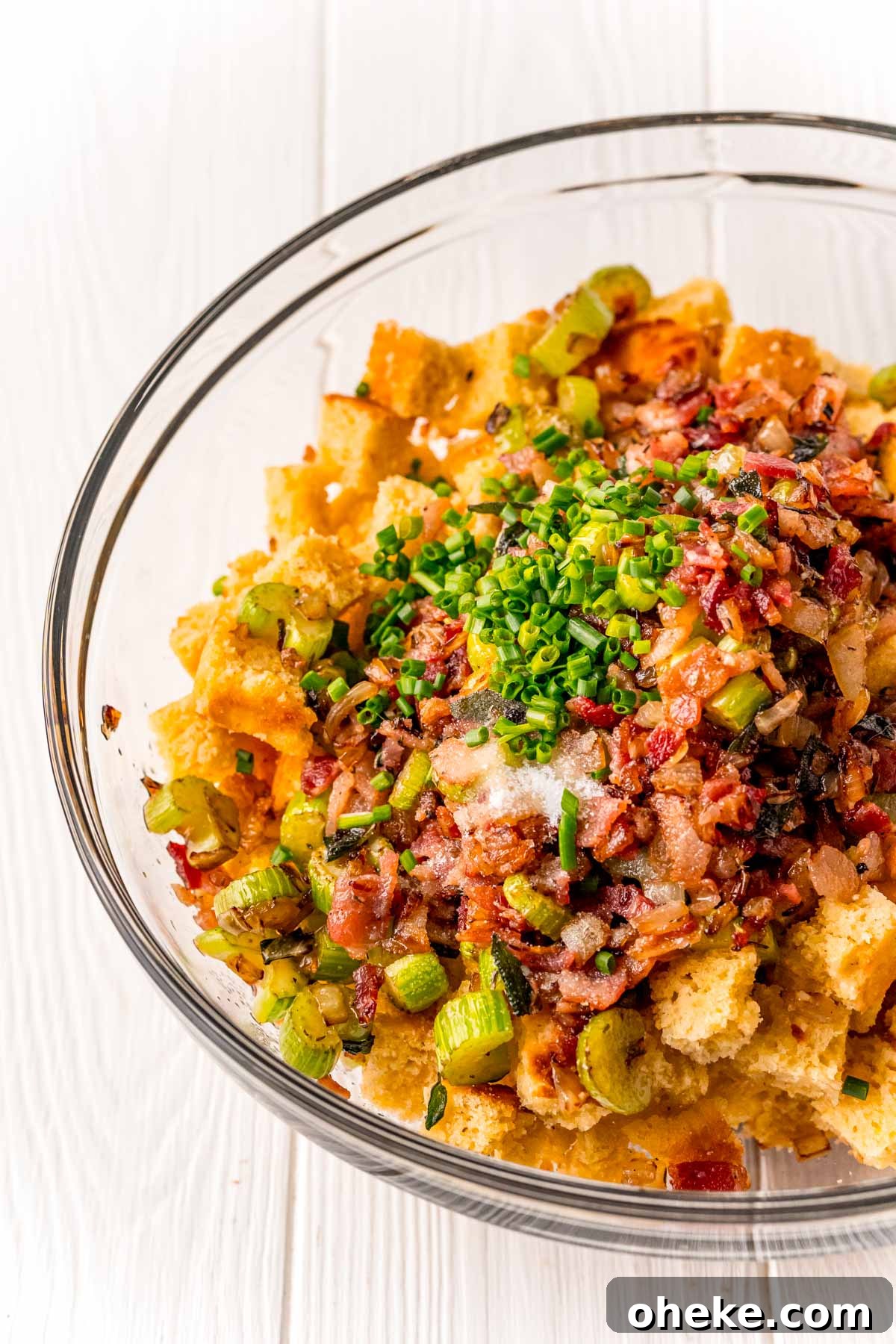 cornbread cubes, celery, onions, bacon, and chives in a glass mixing bowl.