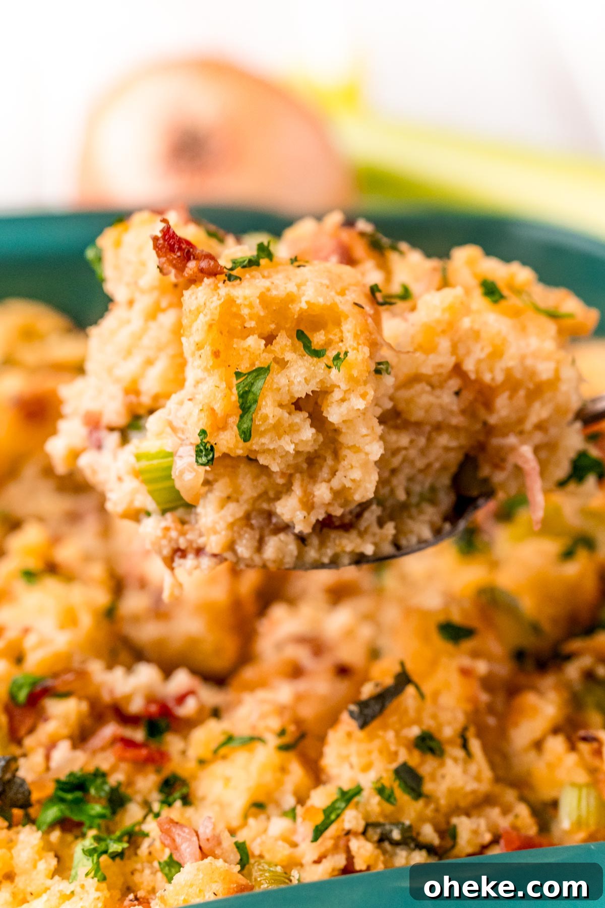 A serving spoon with a scoop of cornbread dressing over a baking dish.
