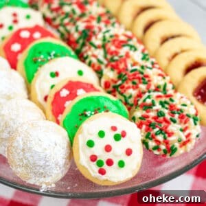 One Cookie Dough, Four Delicious Desserts You Can Make Now 6 powdered sugar covered hidden kiss cookies, frosted Christmas cookies, sprinkle Christmas cookies, and thumbprint cookies with jam on a platter