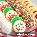 One Cookie Dough, Four Delicious Desserts You Can Make Now 7 powdered sugar covered hidden kiss cookies, frosted Christmas cookies, sprinkle Christmas cookies, and thumbprint cookies with jam on a platter