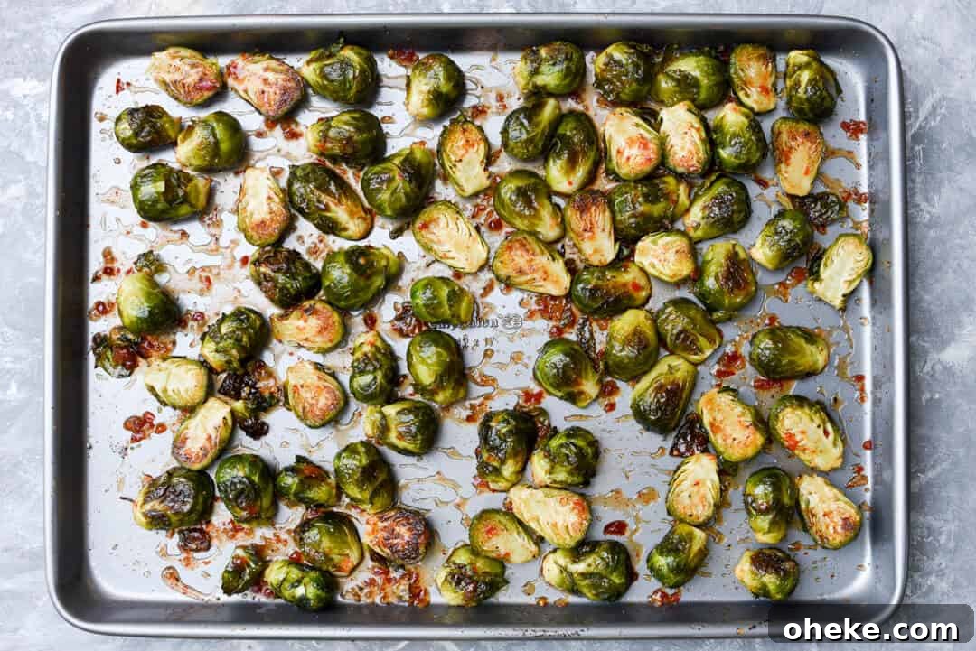 The Brussels sprouts are mixed with chili garlic sauce on the baking sheet.