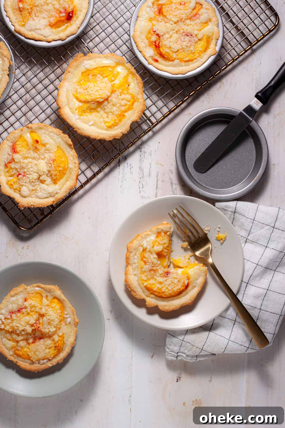 Mini peach custard pies cooling on a rack with a couple portions on plates and a fork cutting into one.
