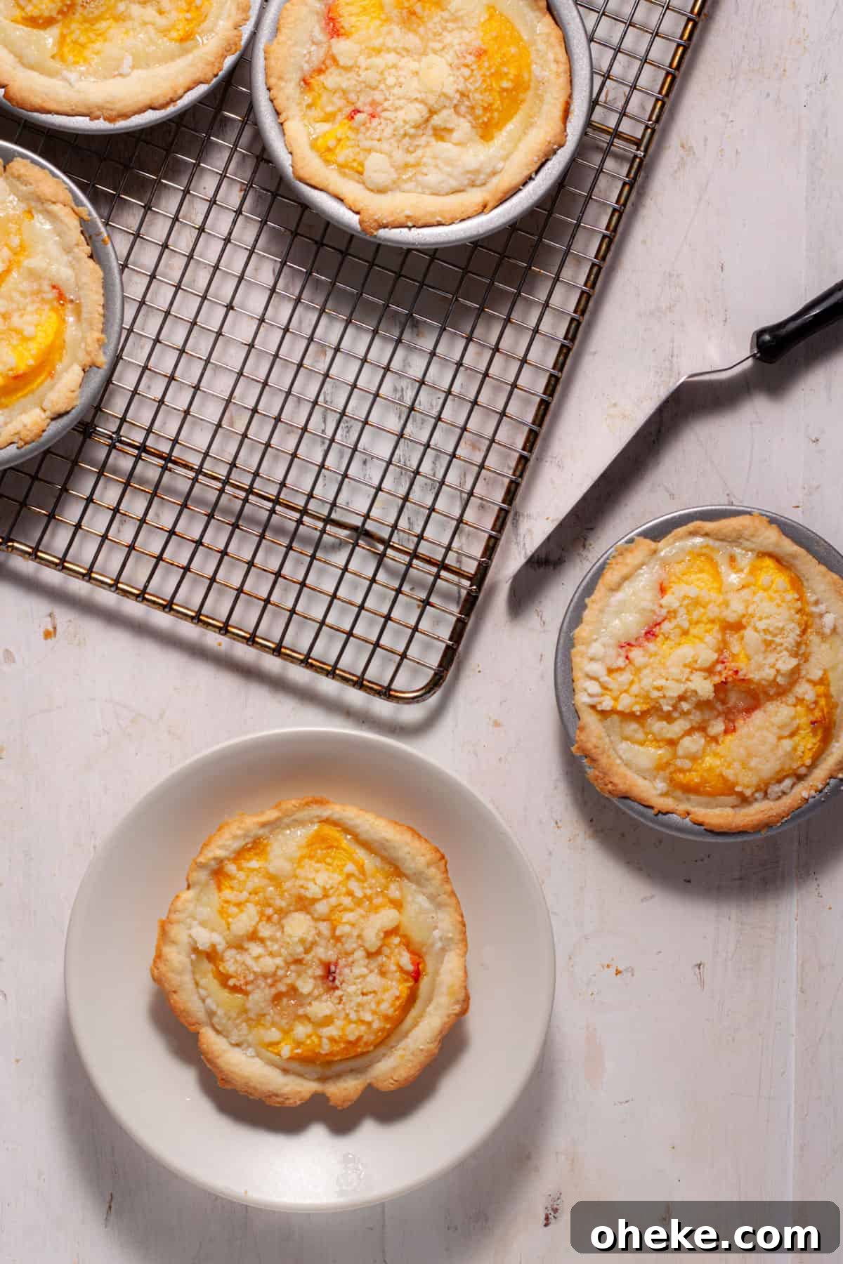 Mini peach custard pies on a small plate and others cooling in the background.