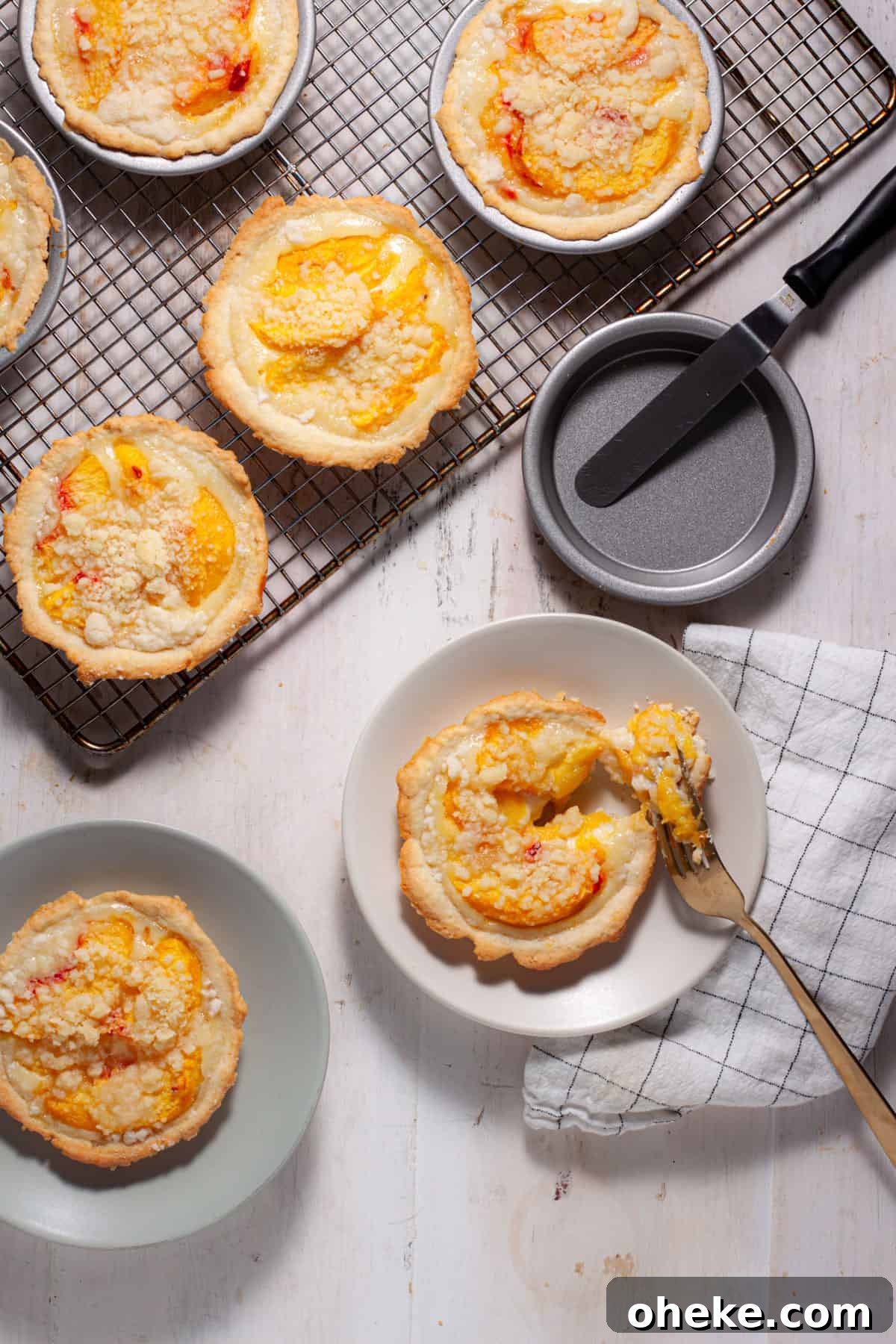 Mini peach custard pies cooling on a rack with a couple portions on plates and a fork cutting into one.
