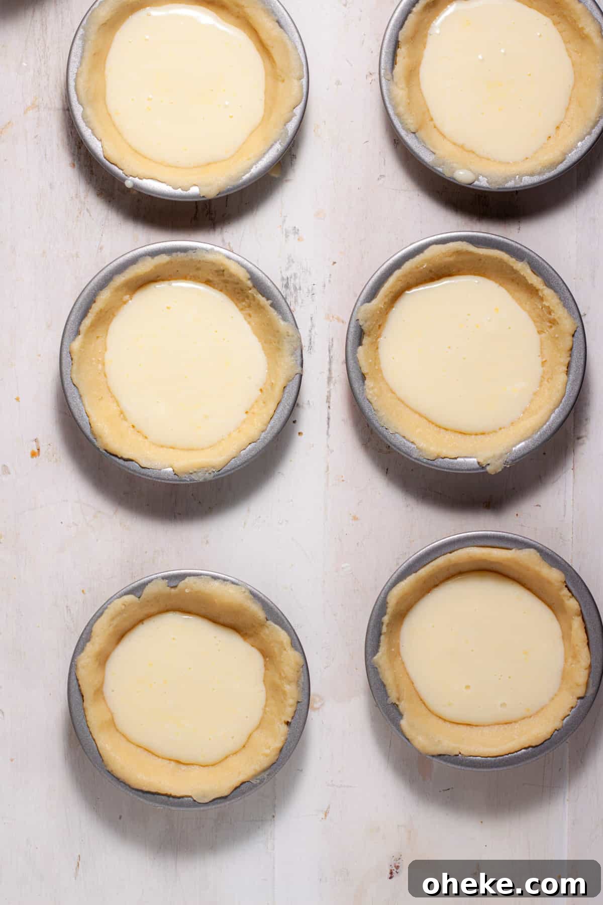 Mini peach custard pies getting assembled with the custard portion poured into the unbaked pie crust.