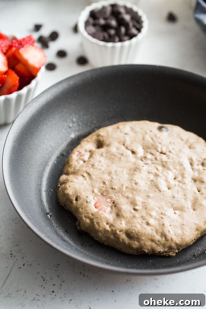Strawberry Chocolate Chip Buckwheat Pancakes Recipe 6 Up-close view of a Strawberry Chocolate Chip Buckwheat Pancake cooking in a skillet.