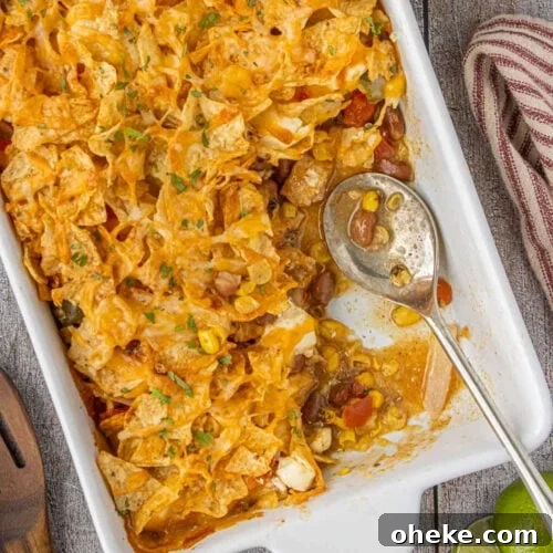 Baked 7 layer Tex-Mex chicken casserole topped with crunchy tortilla chips and melted cheese in a white casserole dish.