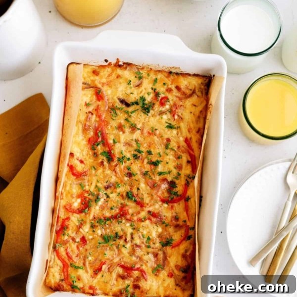 Baked casserole with red peppers and herbs in a white dish, surrounded by eggs, apples, orange juice, and a glass of milk on a table.