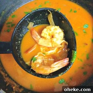 Prawn curry held up in ladle with two prawns visible
