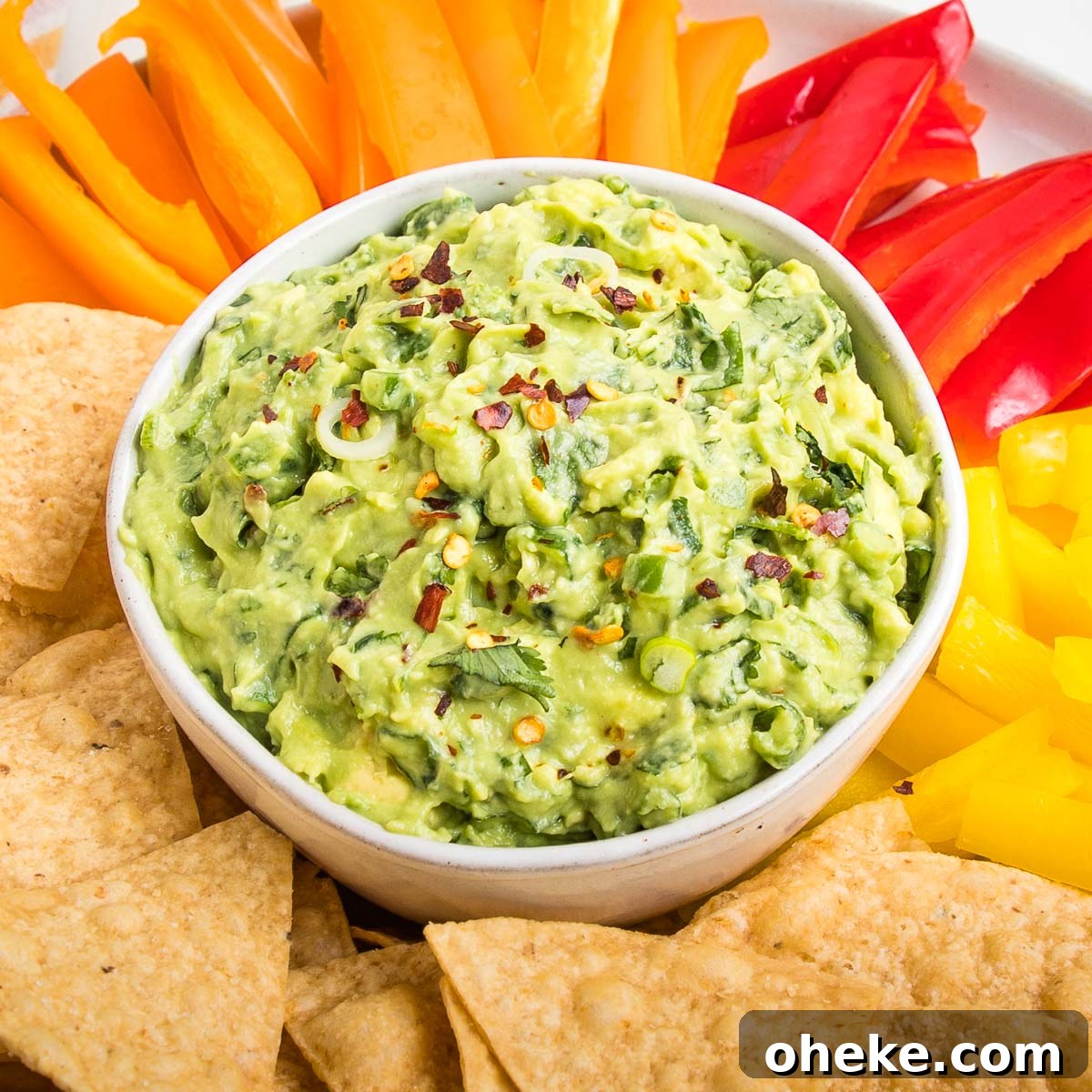 Close up of a bowl of chunky vegan guacamole sprinkled with red pepper flakes.