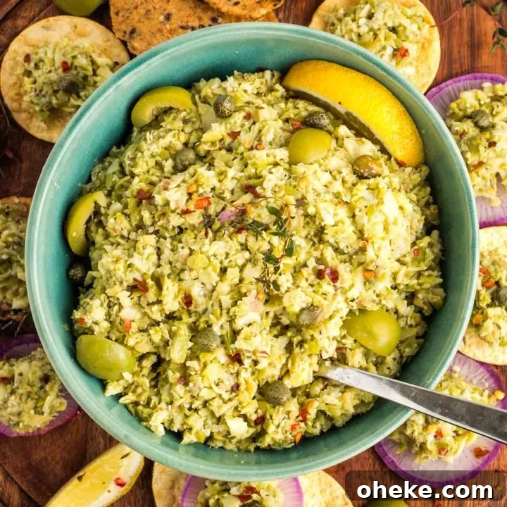 Bowl of green olive tapenade with capers and lemon, surrounded by crackers and radish slices.