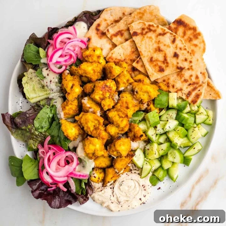 Tofu shawarma on a plate with pita, cucumbers, hummus, pickle red onions and leafy greens.
