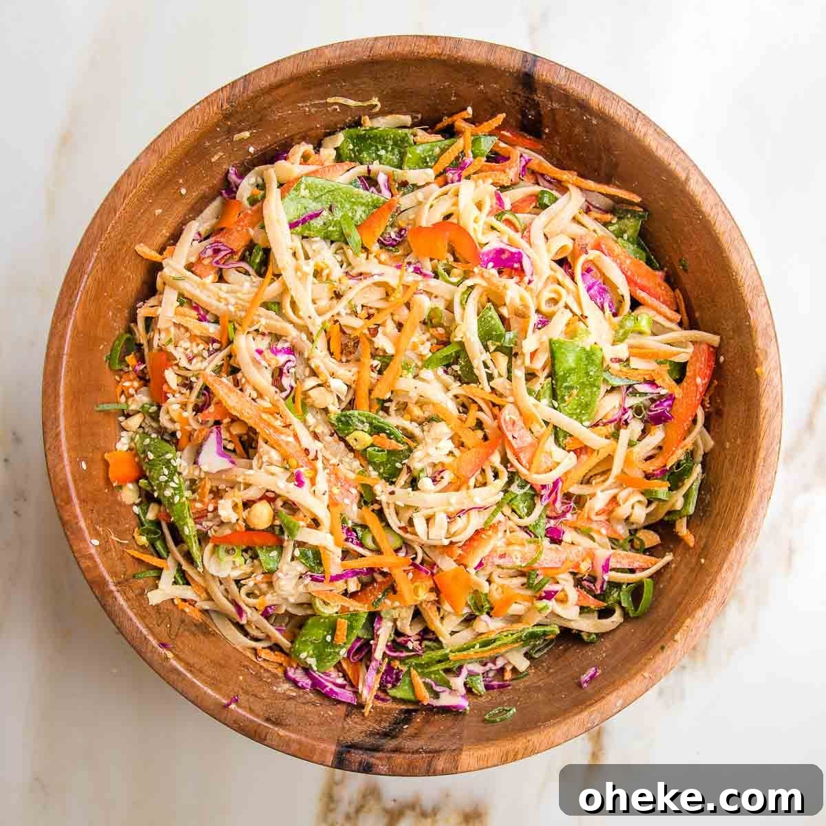 Wooden bowl with rice noodles and crunchy vegetables tossed with tahini dressing.