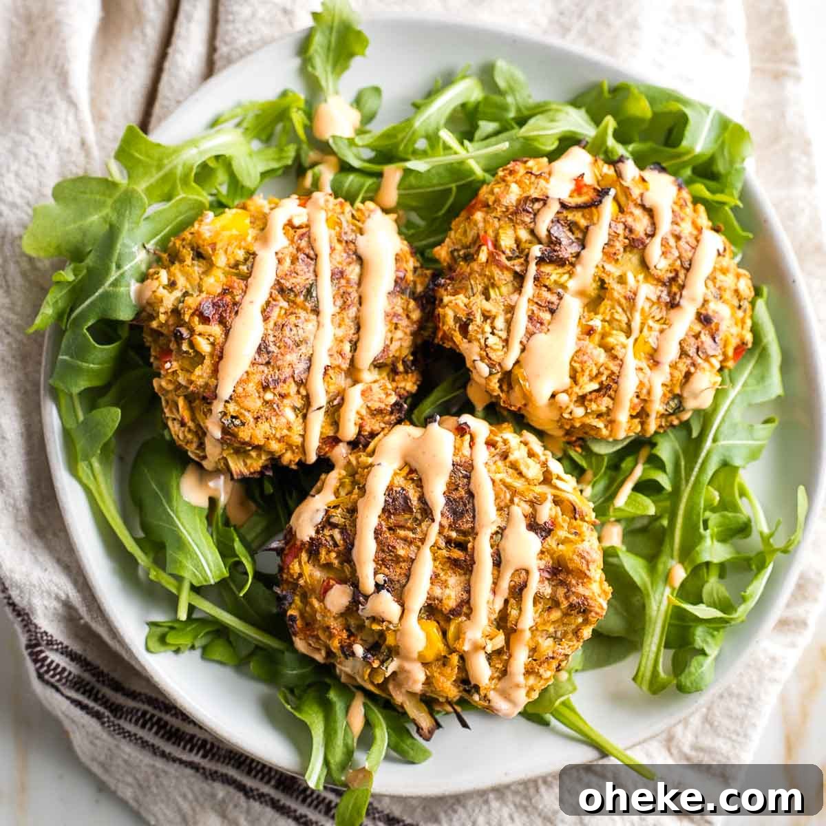 Three vegan crab cakes set atop arugula and drizzled with sriracha tahini.