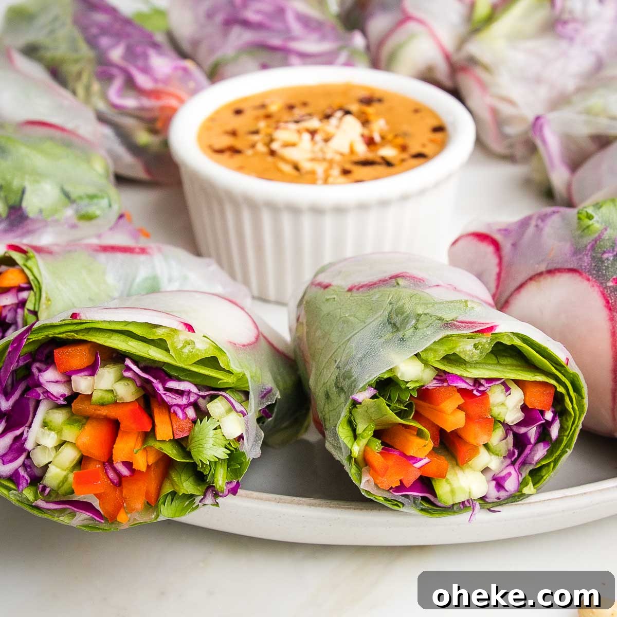 Fresh spring rolls cut in half with colorful julienned veggies shown and a small dish of peanut sauce.