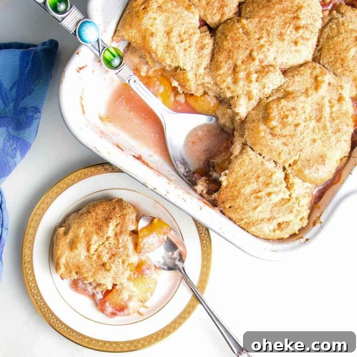 Serving of peach cobbler on a china plate with baking dish in the background.