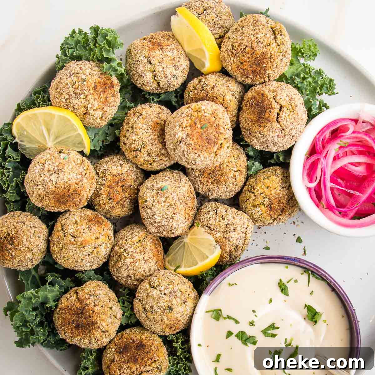 plate filled with baked falafel balls, tahini sauce and small bowl of pickled onions.