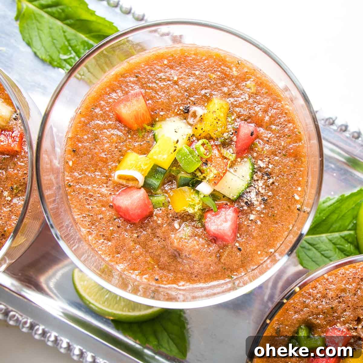Close up of a glass filled with watermelon gazpacho with small diced, colorful veggies and cracked black pepper.