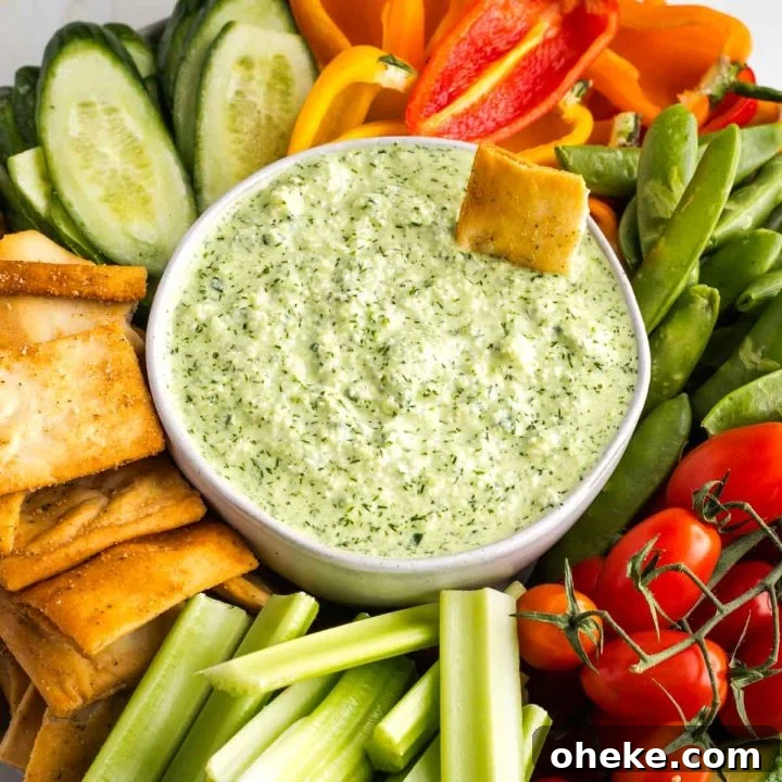 Creamy green dip in a bowl, surrounded by colorful vegetables.