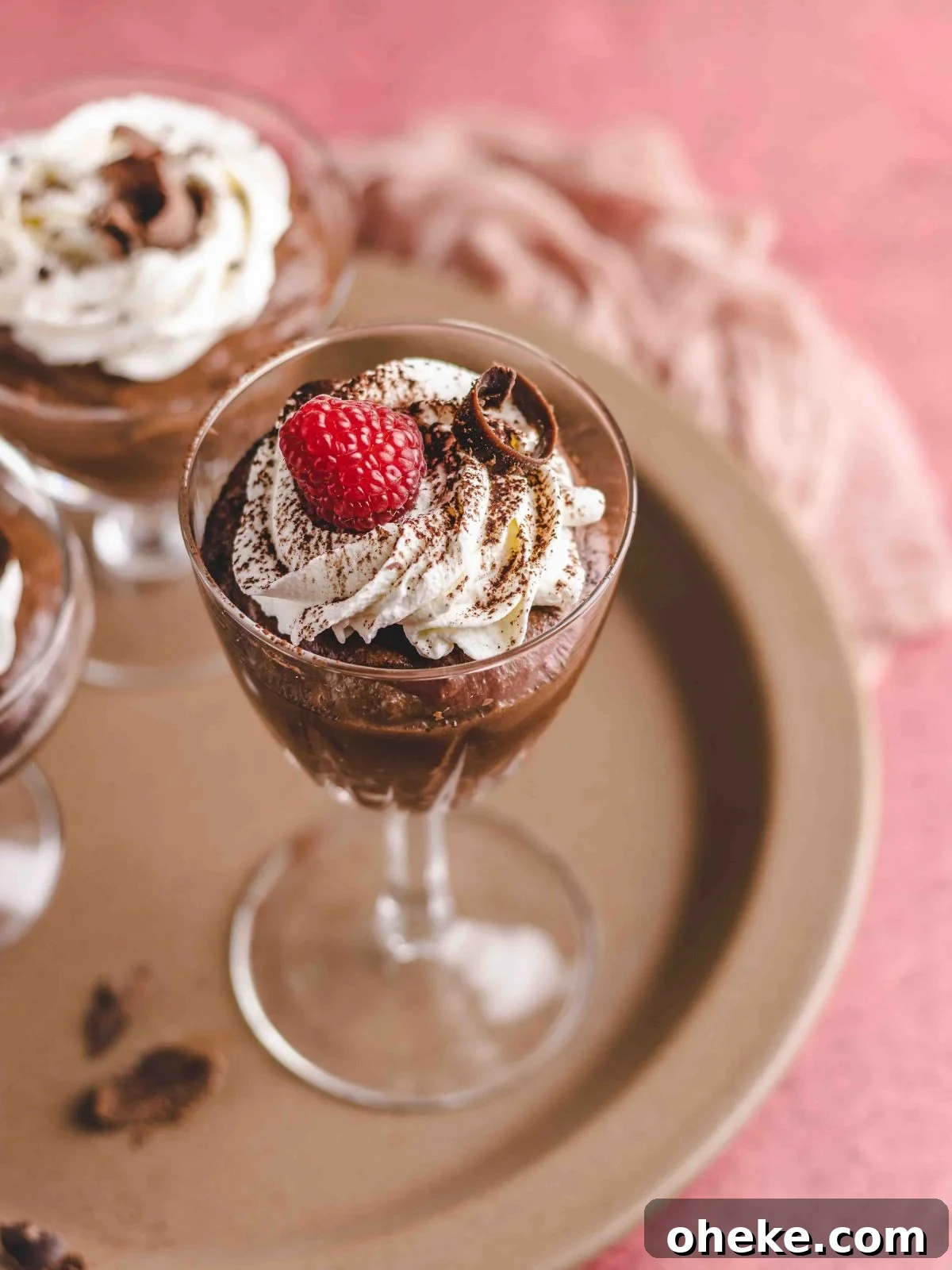 Chocolate mousse in a tall glass garnished with raspberry and cocoa powder.