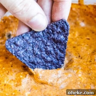 Hand dipping chip into chili cheese dip.