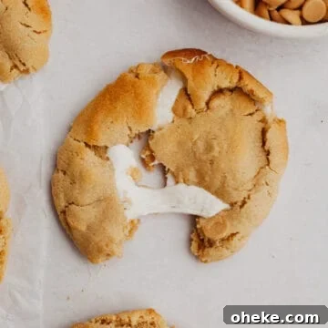 A peanut butter cookie stuffed with marshmallow on parchment paper.