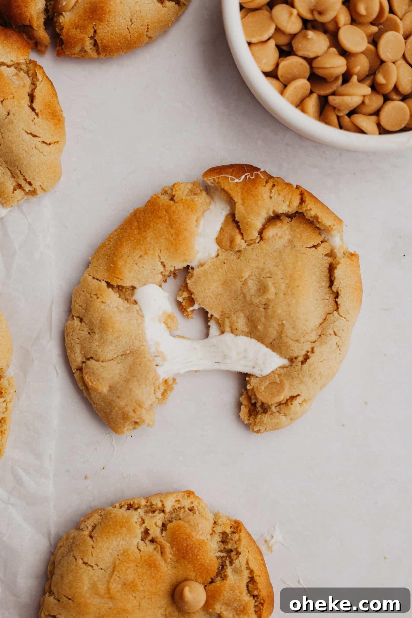 A peanut butter cookie stuffed with marshmallow on parchment paper.