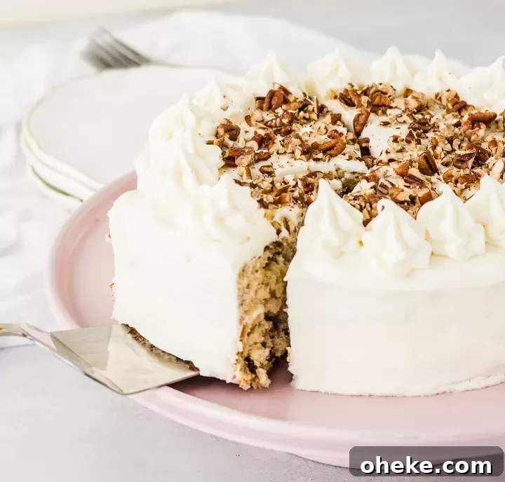 cake server taking a slice of cake mix hummingbird cake off of a cake stand with a stack of plates in the background