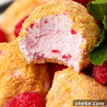 Raspberry cheesecake bites coated in graham cracker crumbs stacked on a plate.