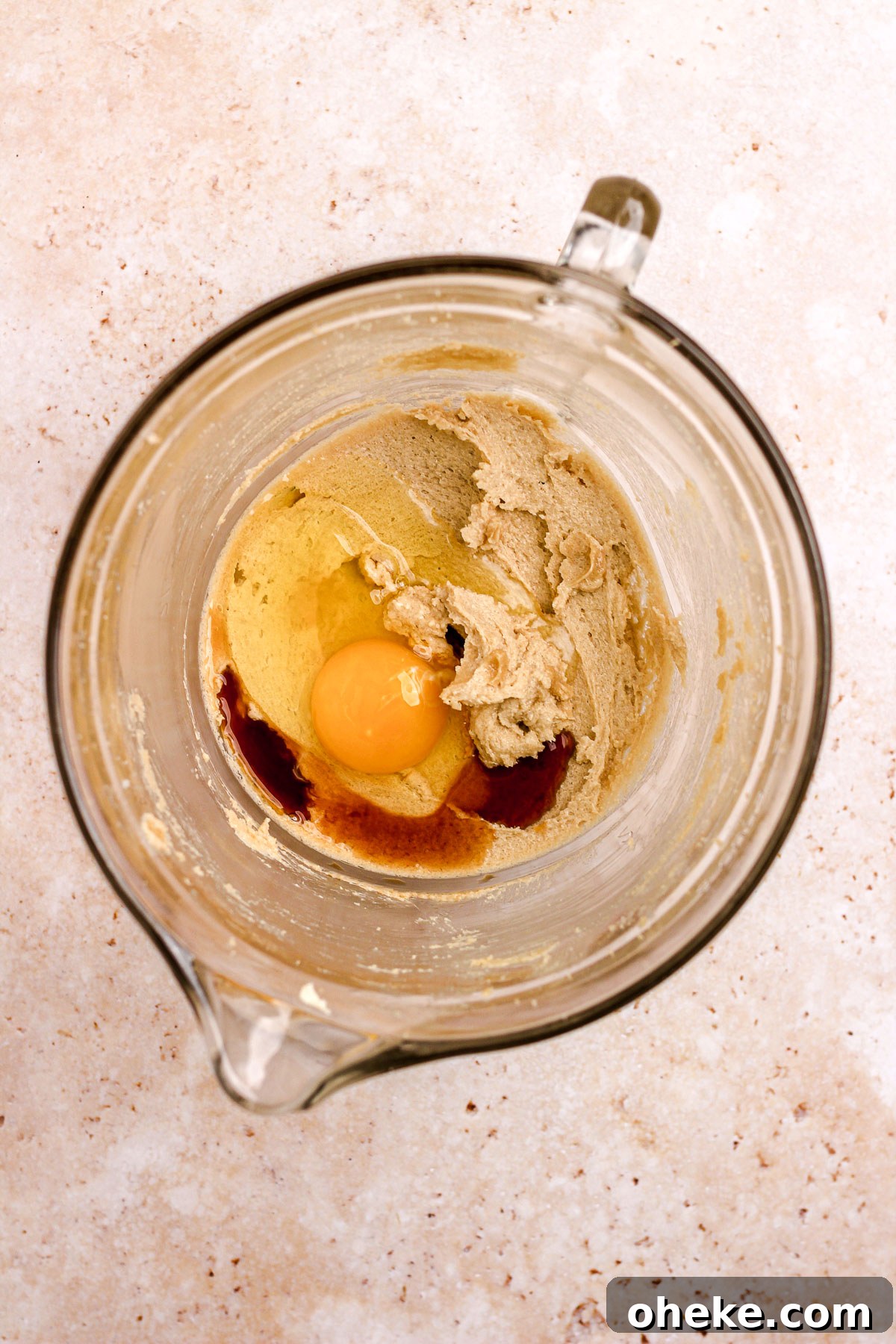 A glass bowl of creamed sugar and butter with an egg and vanilla for cookie dough.